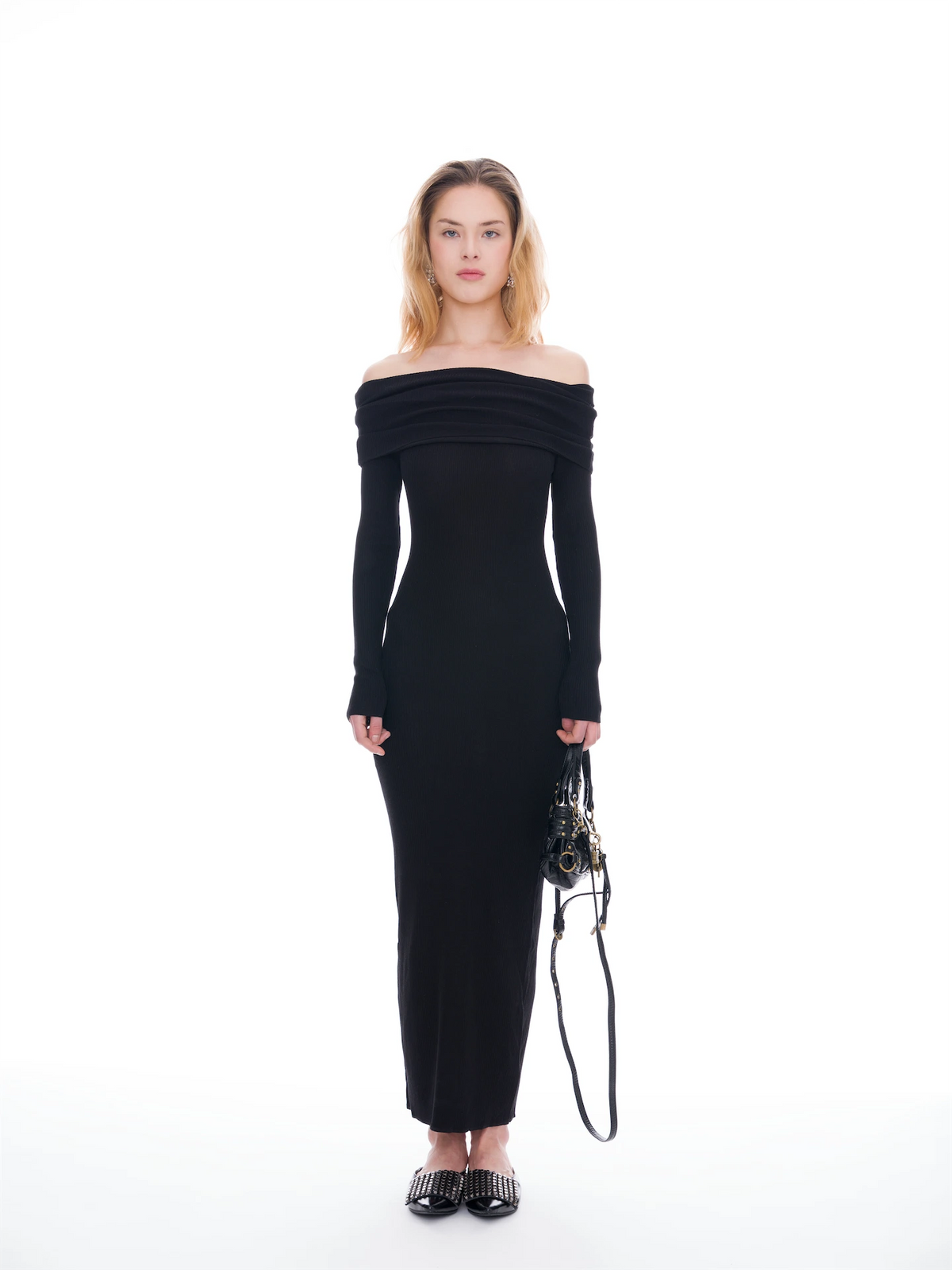 Woman wearing a black off-shoulder dress holding a bag on a white background