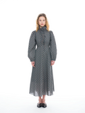A model stands against a white studio background wearing a long-sleeved midi dress with a high mock neck, gathered waist, and an all-over geometric pattern in blue, orange, and gray.