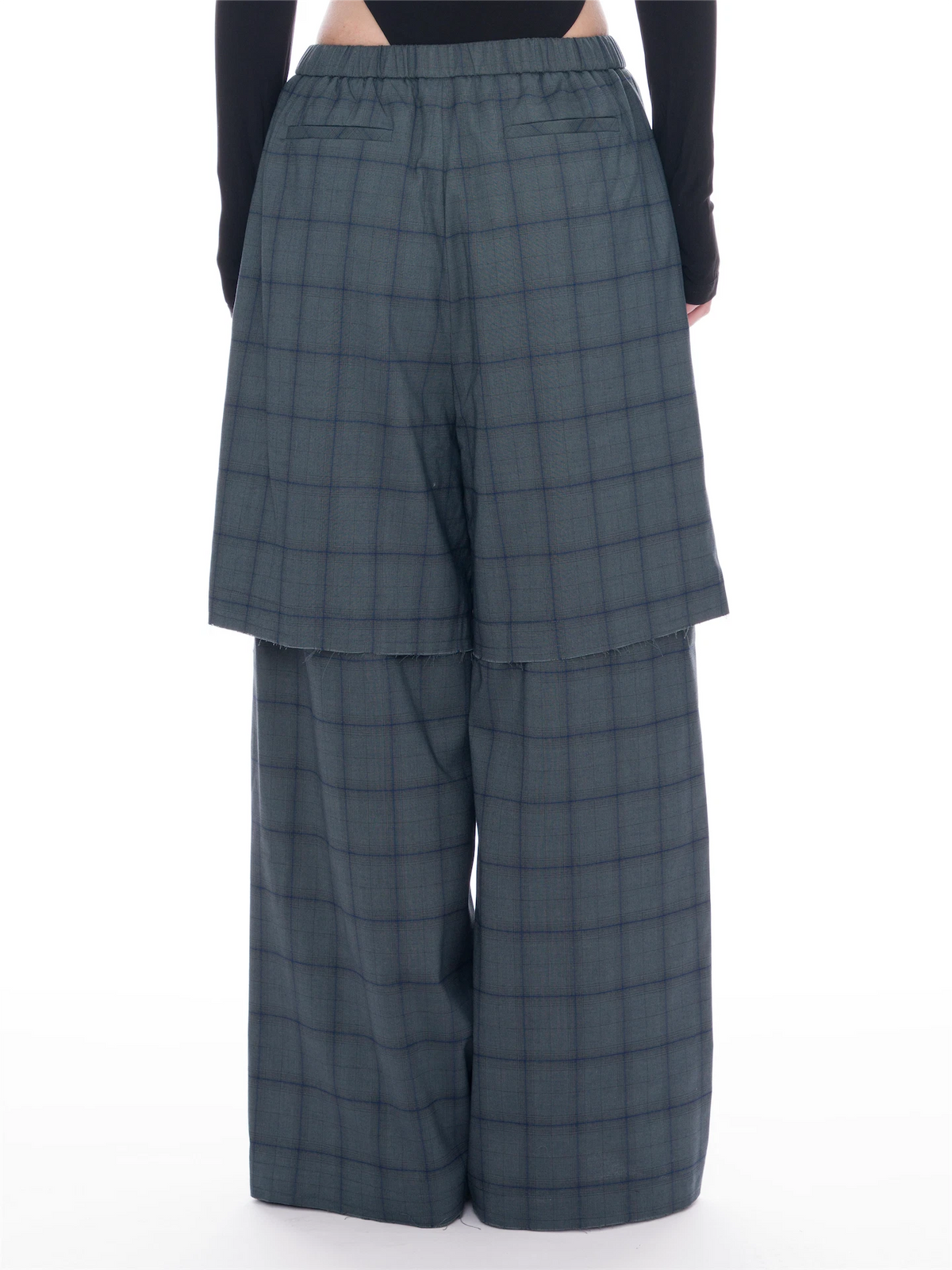 A model is shown from the waist down wearing wide-leg, high-waisted plaid trousers in a muted slate gray with a subtle blue undertone. The pants feature a button-up front and a draped, layered design.