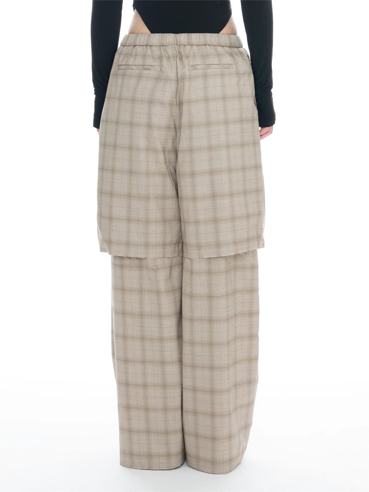 A person shown from the back wearing wide-leg plaid trousers in beige and brown with a black long-sleeve top, against a plain white studio background.