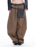 A model is shown from the waist down wearing wide-leg brown cargo pants with a black belt, a black utility pouch, and black studded shoes against a white background.