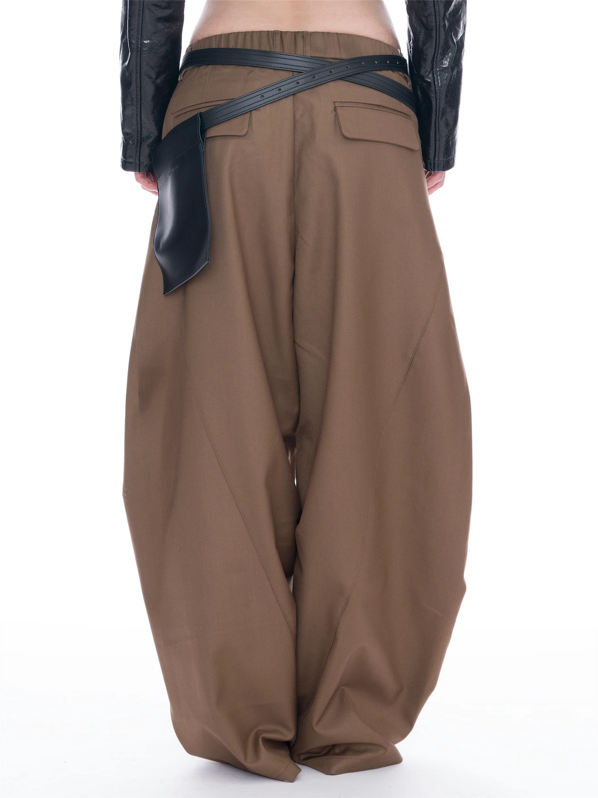 A person shown from the back wearing very loose, wide-leg brown pants with a black leather belt and matching black leather side detail, against a plain white studio background.