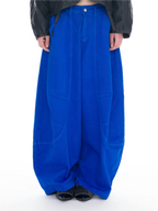 A person wearing extremely baggy, wide-leg blue pants with a black jacket and black shoes, photographed from the waist down against a plain white background.