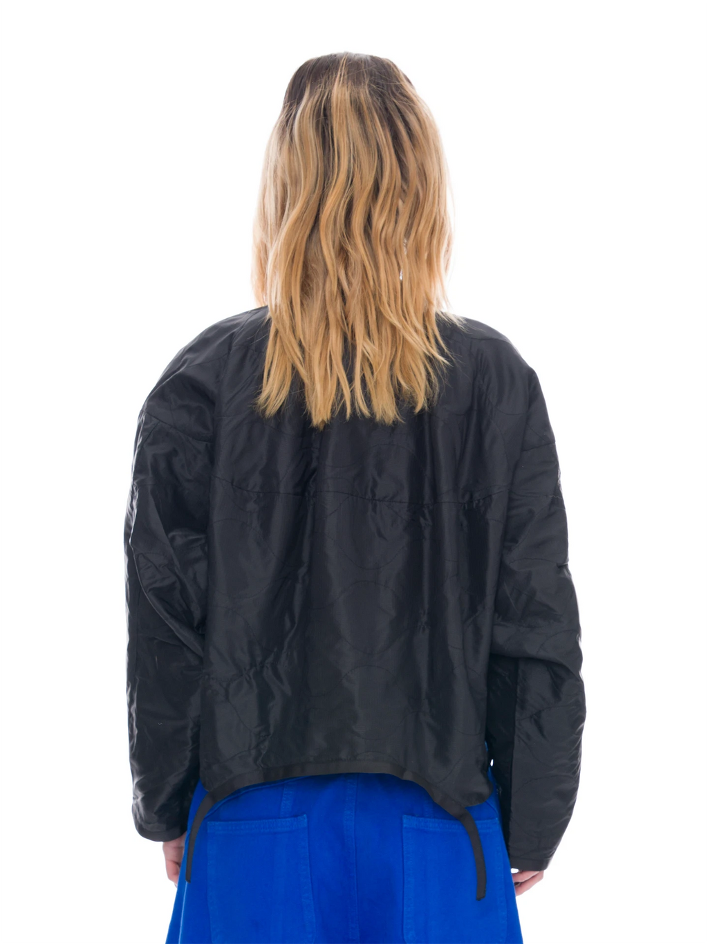 A person shown from the back wearing a black cropped jacket and bright blue bottoms against a plain white studio background.