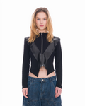 A model wearing a black asymmetrical zip-front jacket with glossy black paneling and blue denim jeans, photographed against a solid white background.