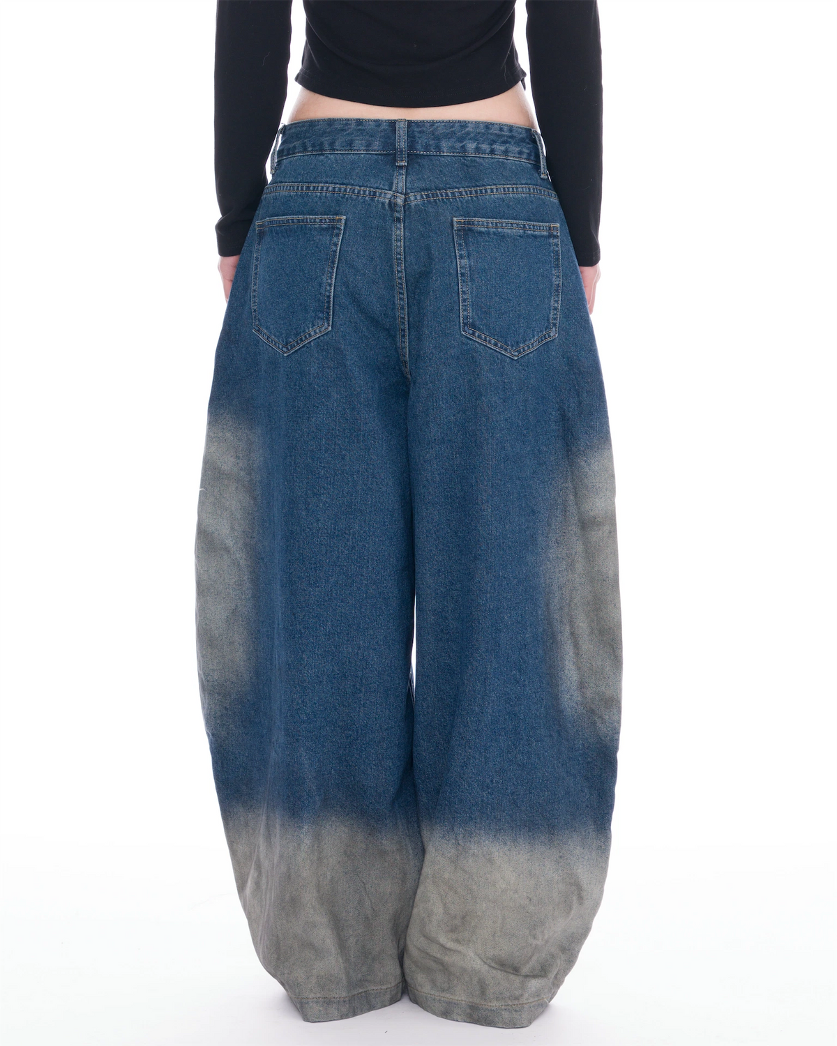 A person viewed from the back wearing very wide-leg blue denim jeans with a faded gray tie-dye effect concentrated at the lower legs, paired with a black long-sleeve top against a plain white background.