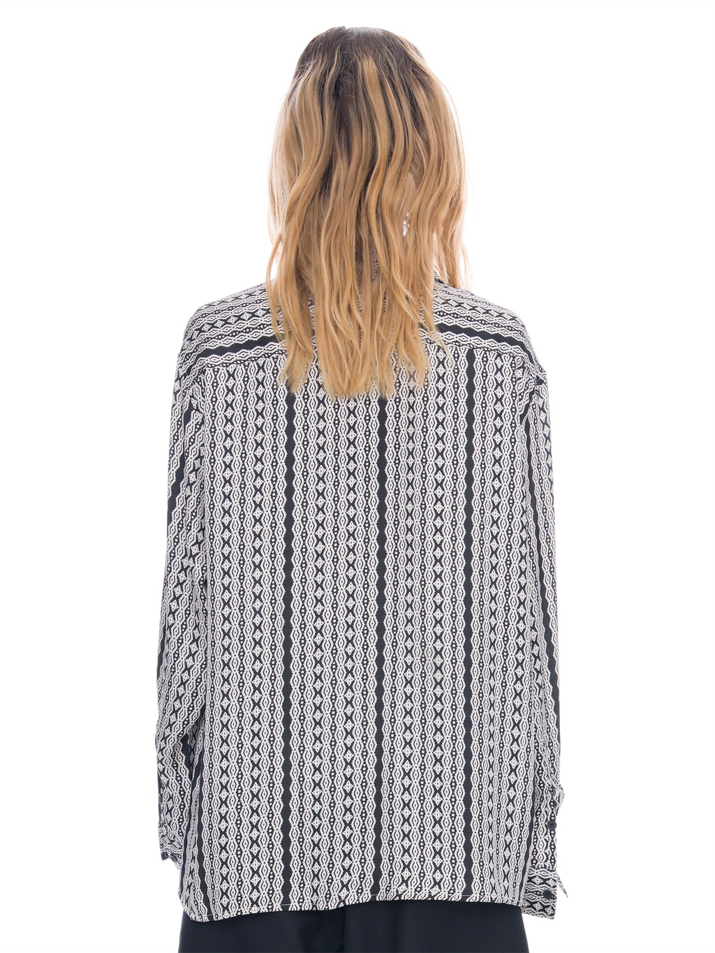 A woman viewed from the back wearing a loose-fitting long-sleeve button-up shirt with a black and white geometric tribal pattern, set against a plain white background.
