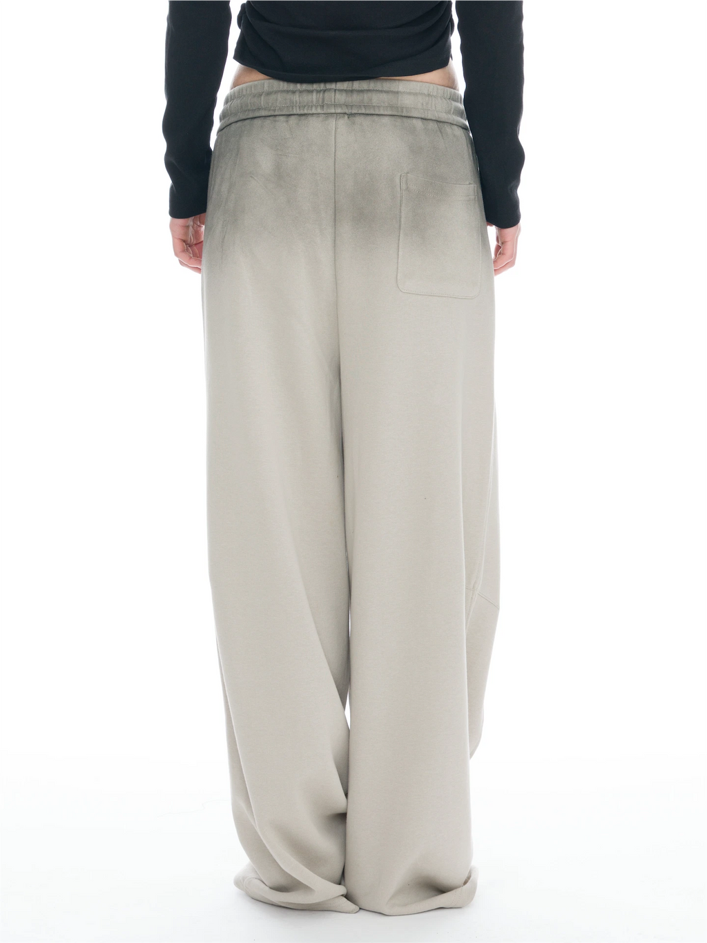 A person shown from the back wearing wide-leg beige pants with a faded wash effect and a black long-sleeve top, against a plain white background.