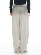 A person shown from the back wearing wide-leg beige pants with a faded wash effect and a black long-sleeve top, against a plain white background.