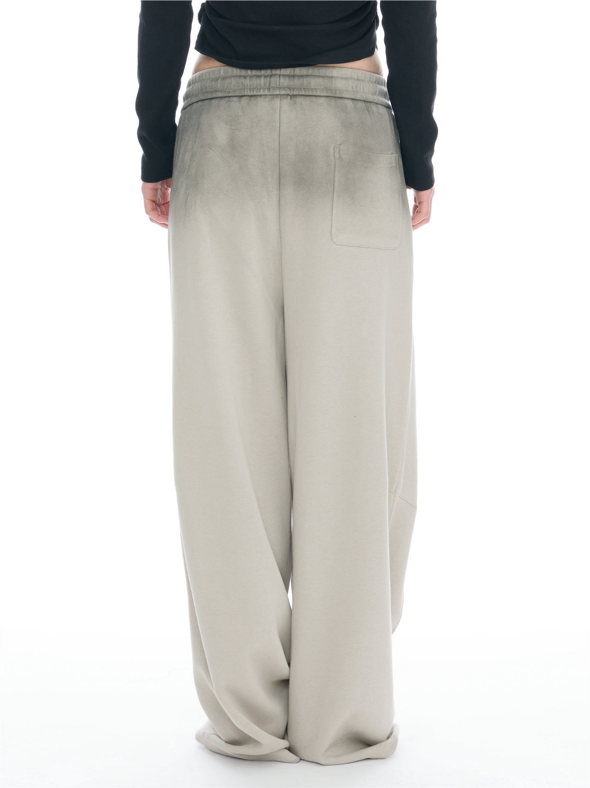 A person shown from the back wearing wide-leg beige pants with a faded wash effect and a black long-sleeve top, against a plain white background.