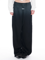 A person wearing wide-leg, floor-length pants with a smooth gradient colour transition from faded black at the top to black at the bottom, styled with a black cropped long-sleeve top and black studded flat shoes against a white studio background.
