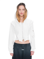 A model wearing a white cropped zip-up hoodie with a high hood, paired with distressed blue jeans and a black studded belt, against a solid white background.