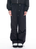 A person wearing black wide-leg cargo pants with a drawstring waist, paired with a black jacket and white-and-black sneakers, photographed against a plain white studio background.