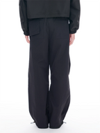 A person shown from the back wearing loose black wide-leg pants with large back patch pockets and a black cropped jacket, photographed against a clean white studio background.
