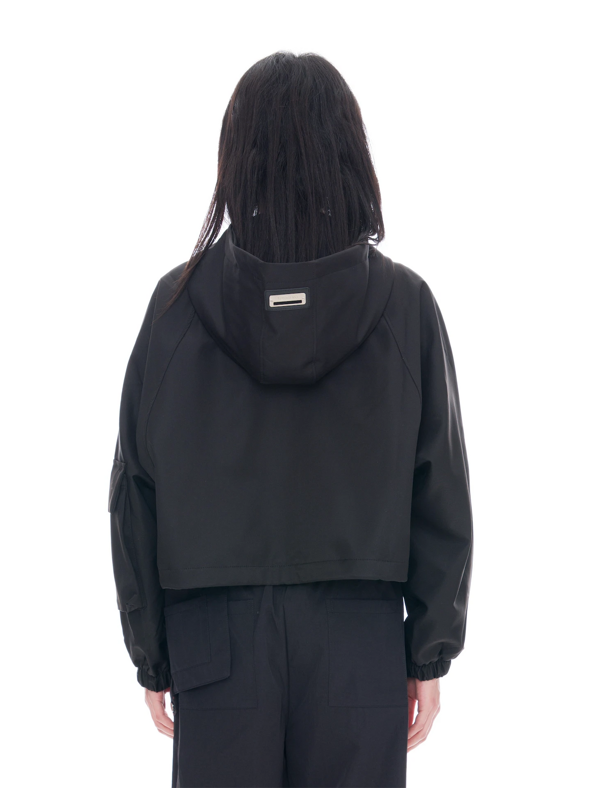 A model shown from the back wearing a black cropped hooded jacket and matching black cargo pants against a solid white background.