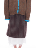 A person wearing a brown knit cardigan with bright blue lace trim, a dark brown and black vertically striped skirt, and a white pleated skirt with a lace hem, shown against a plain white background.