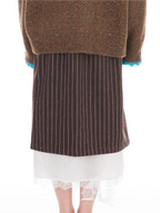 A person shown from the back wearing a brown knit sweater with blue trim, a dark brown pinstriped skirt, and a white pleated skirt with lace hem.