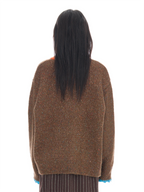 Back view of a person with long black hair wearing an oversized brown knit sweater with multicolored flecks and blue ribbed cuffs, against a plain white background.