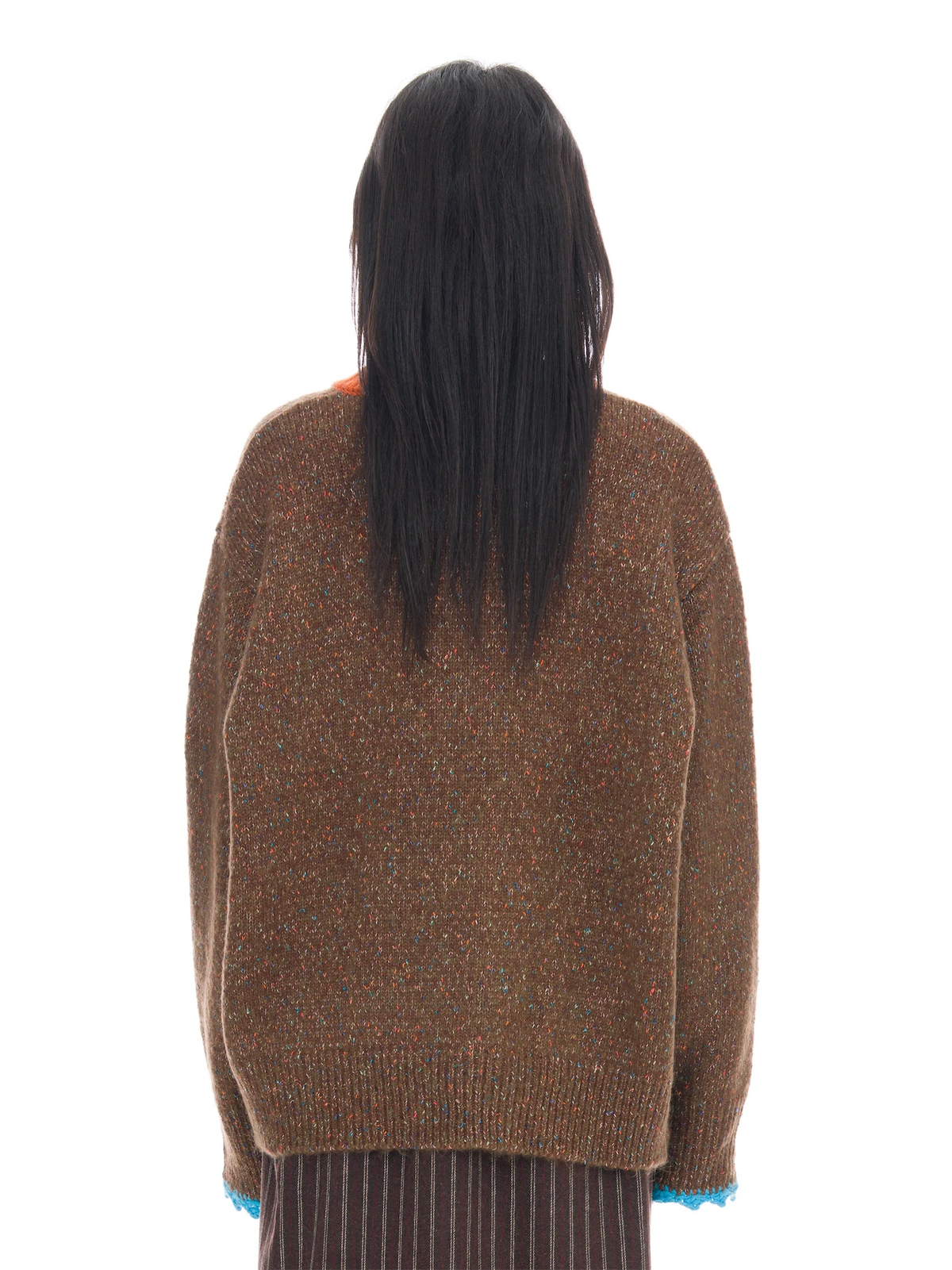 Back view of a person with long black hair wearing an oversized brown knit sweater with multicolored flecks and blue ribbed cuffs, against a plain white background.