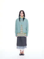 A model stands against a solid white background wearing a light teal-green zip-up sweater layered over a striped knit top, a dark gray pinstriped skirt, and black flat shoes.