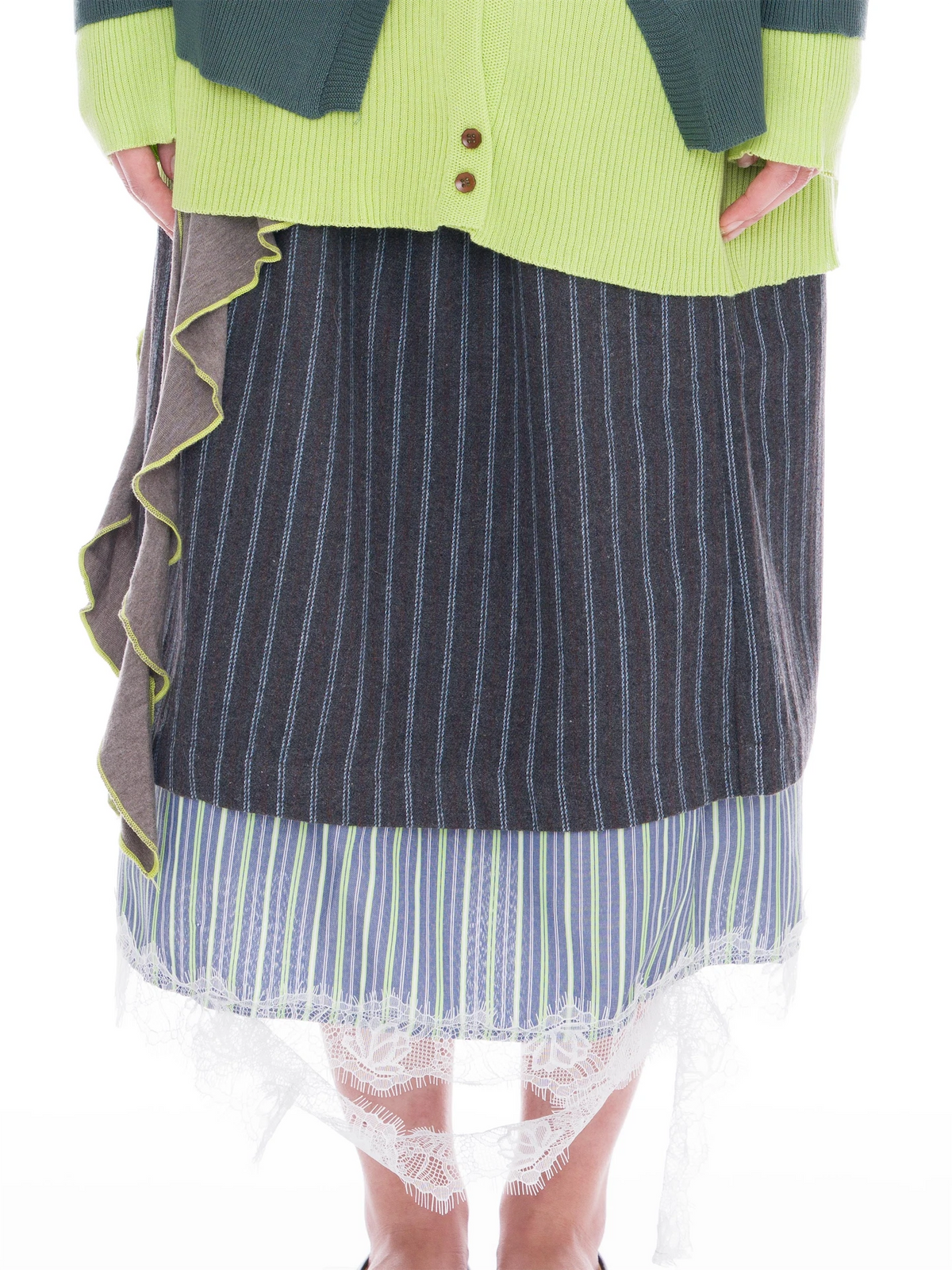 A person wearing a layered skirt with a dark gray and white pinstripe main body, a blue and white striped underlayer, a white lace hem, and a brown ruffled side panel, styled with a lime green cardigan.