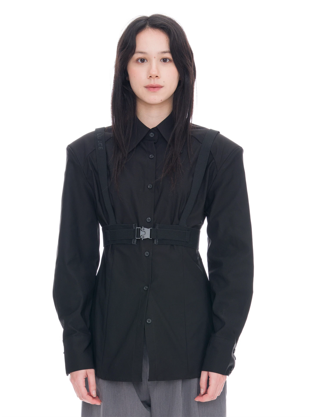 A model wearing a black long-sleeve button-up shirt with structured shoulders, a matching waist belt with a silver buckle, and gray trousers, shot against a solid white background.