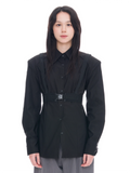A model wearing a black long-sleeve button-up shirt with structured shoulders, a matching waist belt with a silver buckle, and gray trousers, shot against a solid white background.
