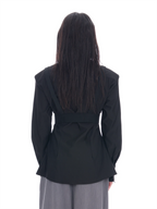 A person viewed from the back wearing a black long-sleeve belted jacket and light gray wide-leg pants against a plain white background.