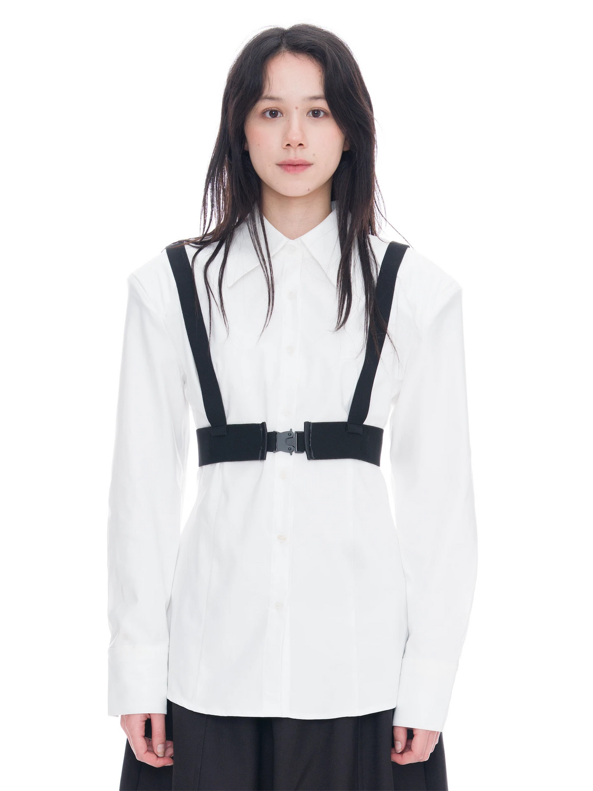 A model wearing a white long-sleeve button-up shirt with black suspenders and a black waist belt, paired with a black skirt, shot against a solid white background.