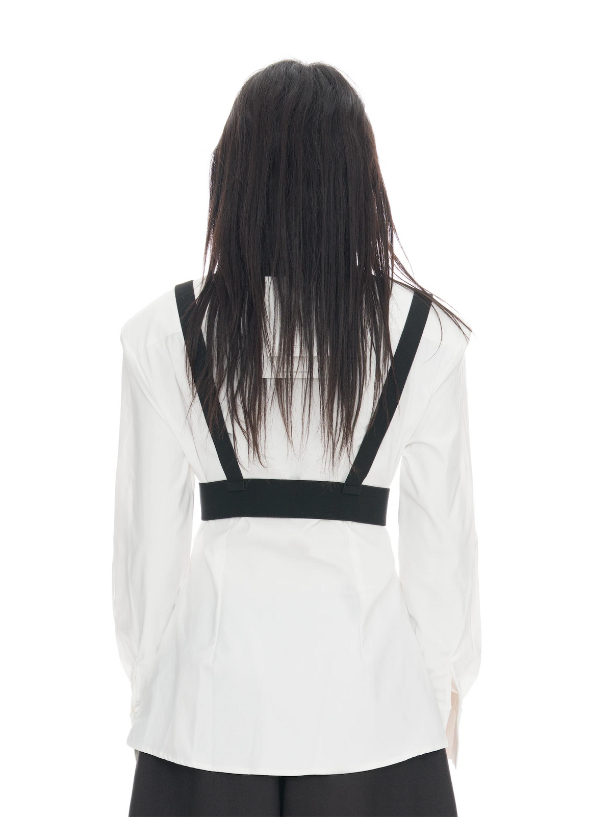 A person viewed from the back wearing a white long-sleeve blouse with black shoulder straps and a black horizontal band across the upper back, paired with black bottoms, against a plain white studio background.