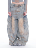 A model is shown from the waist down wearing extremely baggy, oversized light blue washed denim cargo pants with large side flap pockets and a faded tan wash on the front.