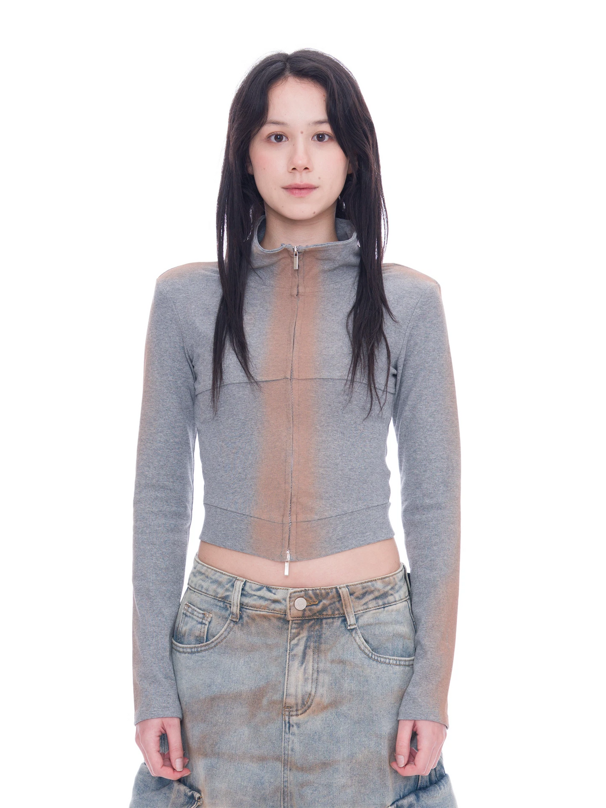 A model wearing a gray long-sleeve cropped zip-up top with sheer mesh side panels and light-wash denim jeans, standing against a solid white background.