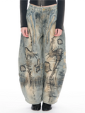 A person wearing extremely baggy distressed denim pants with abstract black painted markings, a black long-sleeve top, and black shoes, photographed against a plain white studio background.