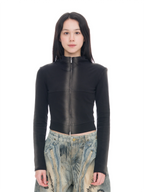 A model stands against a seamless white studio background wearing a fitted black long-sleeve top with a high collar and a full-length front zipper, paired with extremely baggy wide-leg pants in a beige, blue, and gray abstract landscape print, and black shoes.