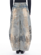 A pair of wide-leg, voluminous light-wash denim pants with distressed patches, raw edges, and black graphic line embroidery near the hems, shown on a model from the back against a white background.