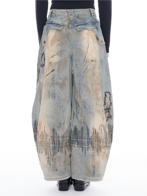 A pair of wide-leg, voluminous light-wash denim pants with distressed patches, raw edges, and black graphic line embroidery near the hems, shown on a model from the back against a white background.