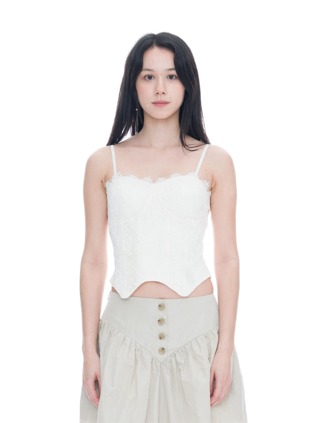 A woman modeling a white lace-trimmed camisole top with a corset-style waist, paired with a light beige skirt, against a solid white background.