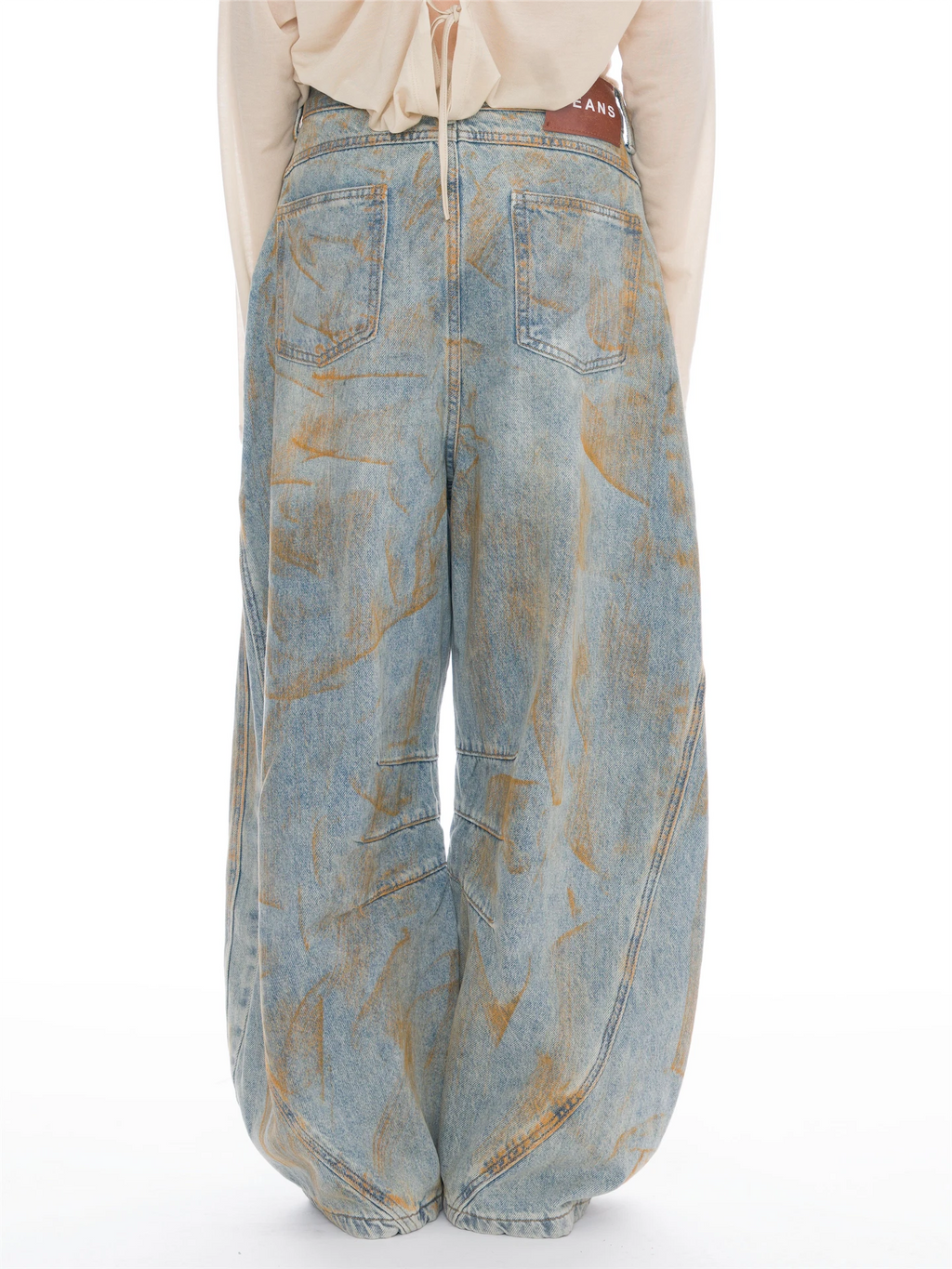 Wide-leg light blue denim jeans with a distressed tan wash pattern, shown from the back on a model wearing a cream top against a white background.