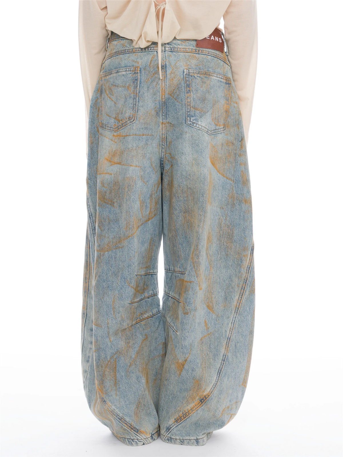 Wide-leg light blue denim jeans with a distressed tan wash pattern, shown from the back on a model wearing a cream top against a white background.