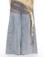 Light-wash wide-leg denim shorts with a sheer dark gray mesh overlay draped over the waist and a yellow underlayer, shown against a plain white background.