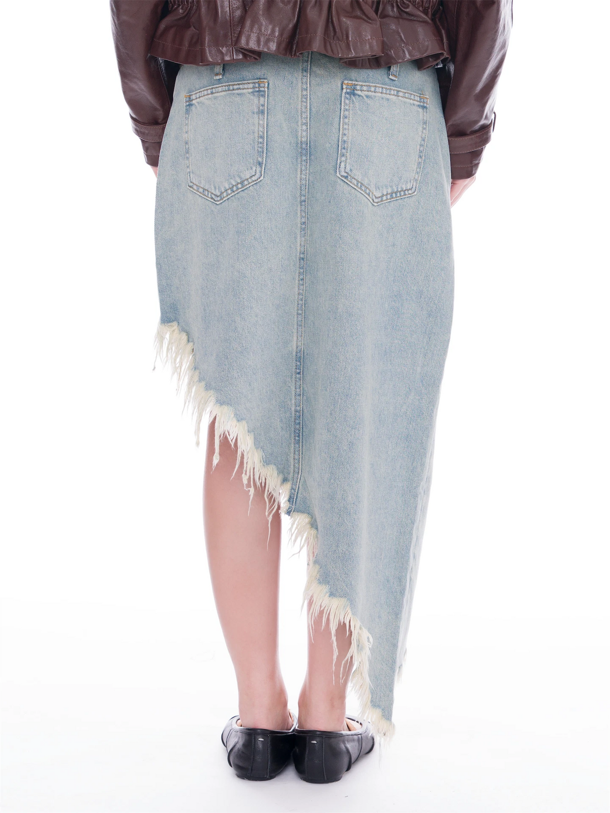 A person shown from the back wearing a light blue denim asymmetrical skirt with frayed edges, paired with a dark brown jacket and black flats, against a plain white background.