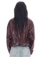 Rear view of a model with long dark hair wearing a brown sheep skin jacket with an elasticated back hem and light blue denim jeans, set against a plain white background.